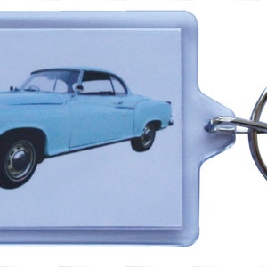以下が含まれることがあります： 銀色のキーリングが付いた薄い青色のビンテージカーのキーホルダー。車は白い背景にクラシックなクーペです。