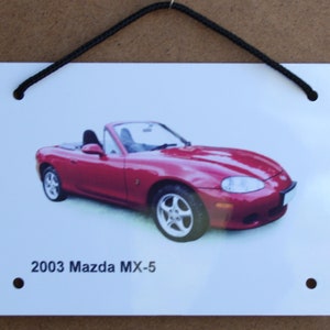 May include: A red 2003 Mazda MX-5 convertible sports car on a white background with black hanging string.