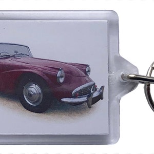 Puede incluir: Un llavero de coche rojo vintage convertible con un anillo de llave plateado. El coche es un diseño clásico con un interior blanco y una capota negra.