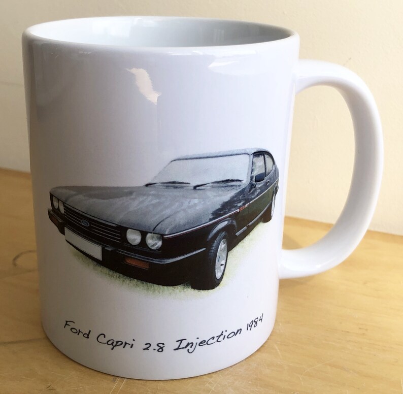 Pu&ograve; includere: Tazza in ceramica bianca con un'illustrazione di una Ford Capri 2.8 Injection 1984 nera e verde.