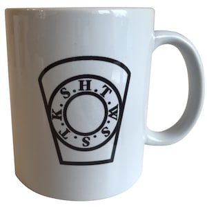 Pode incluir: Caneca de cerâmica branca com um logotipo preto e branco com o texto "K.S.H.T.W.S.S." em um círculo.