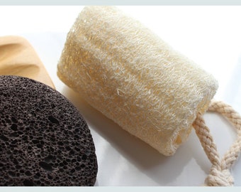 May include: A close-up of three bath and body products: a loofah sponge with a rope handle, a brown pumice stone, and a wooden soap dish.