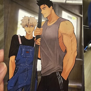 May include: Illustration of two male figures. One is in a grey vest and black athletic trousers. The other wears blue dungarees over a black top. The background is a blurred depiction of a public space.