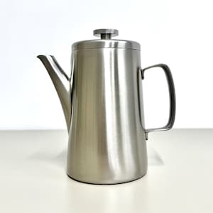 May include: A stainless steel coffee pot with a long spout and a handle. The pot has a lid and a brushed metal finish. The coffee pot is sitting on a white surface.