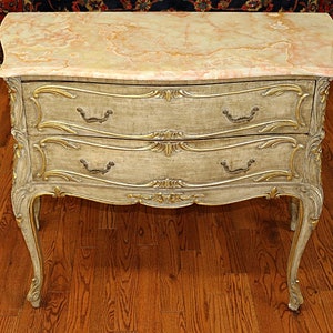 May include: A two-drawer chest with a curved front and ornate gold accents. The chest is made of wood and has a marble top.
