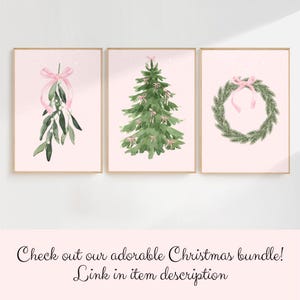 May include: Three framed watercolor prints with a Christmas theme. The prints feature a sprig of mistletoe with a pink bow, a Christmas tree adorned with pink bows, and a wreath with a pink bow. The background is a soft pink color.