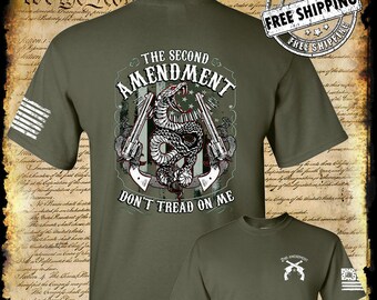 Puede incluir: Una camiseta verde con un gráfico de una serpiente envuelta alrededor de dos pistolas y el texto "The Second Amendment Don't Tread On Me". La camiseta también tiene una pequeña bandera estadounidense en la manga izquierda.