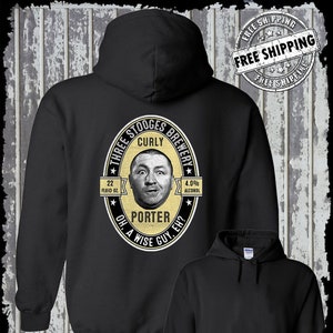 Könnte beinhalten: Schwarzer Kapuzenpullover mit einem gelben und weißen Grafikdruck eines Bierretiketts mit einem Cartoon-Bild von Curly von den Three Stooges. Das Etikett lautet "Three Stooges Brewery" und "Curly" mit einem Cartoon-Bild von Curly. Das Etikett lautet auch "22 Fluid Oz." und "4.0% Alcohol" und "Porter" und "Oh, a wise guy, eh?" Der Pullover hat den Text "Kinsman Trading Co. LLC" unten aufgedruckt.