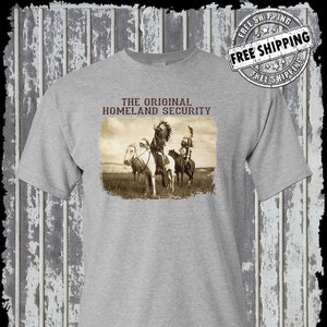May include: A gray t-shirt with a vintage image of three Native American men on horseback. The text "THE ORIGINAL HOMELAND SECURITY" is printed above the image.