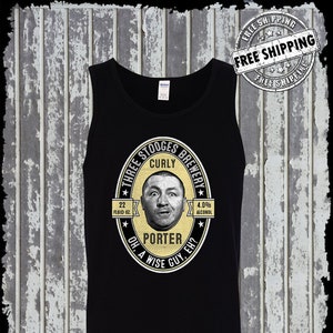 Könnte beinhalten: Schwarzes Tanktop mit einem gelben und weißen kreisförmigen Grafik, das eine Karikatur von Curly von den Three Stooges zeigt. Die Grafik lautet "Three Stooges Brewery", "Curly", "22 Fluid Oz", "4.0% Alcohol", "Porter", "Oh, A Wise Guy, Eh?" und hat auf jeder Seite einen Stern. Das Tanktop hat den Text "Kinsman Trading Co. LLC" unten aufgedruckt.