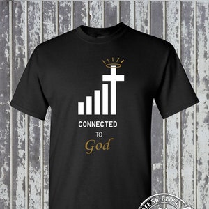 Könnte beinhalten: Schwarzes T-Shirt mit einer weißen Grafik eines Kreuzes mit einem Heiligenschein darüber und einer Signalbalkengrafik darunter. Der Text "CONNECTED TO God" befindet sich unter der Grafik. Das T-Shirt hat ein kostenloses Versandlabel in der unteren rechten Ecke.