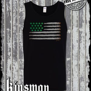 Op de afbeelding: Zwart tanktop met een afbeelding van een Amerikaanse vlag gemaakt van marihuanabladeren en joints. De tekst "Kinsman Trading Co. LLC" staat onderaan het shirt gedrukt.