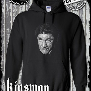 Könnte beinhalten: Schwarzer Kapuzenpullover mit einem weißen Bild von Curly Howard von den Three Stooges. Der Text "Kinsman trading co. llc" ist in weiß am unteren Rand des Pullovers aufgedruckt.