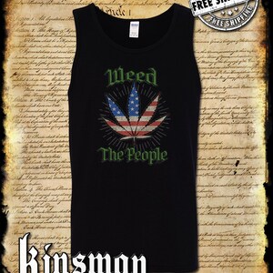 Op de afbeelding: Een zwart tanktop met een ontwerp van een groen marihuanablad. Het blad is gemaakt van rode, witte en blauwe strepen, die lijken op de Amerikaanse vlag. De tekst "Weed The People" is onder het blad gedrukt.