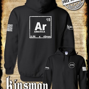 May include: Black hooded sweatshirt with a white graphic of a periodic table element, "Ar" for "America", with the numbers "15", "5.56", and "45mm" printed on it. The sweatshirt has a white "Kinsman Trading Co. LLC" logo on the bottom.