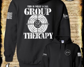 May include: Black hooded sweatshirt with the text "THIS IS WHAT I CALL GROUP THERAPY" above a target graphic. The sweatshirt also features a small American flag design on the sleeve and the text "1776".