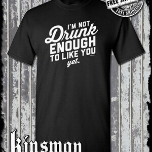 May include: Black t-shirt with the white text "I'M NOT Drunk ENOUGH TO LIKE YOU yet." A "Free Shipping" logo is in the upper right corner. The Kinsman trading co. logo is at the bottom.
