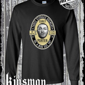 Könnte beinhalten: Schwarzes Langarm-T-Shirt mit einem gelben und weißen kreisförmigen Grafik, das ein Porträt von Curly von den Three Stooges zeigt. Die Grafik lautet "Three Stooges Brewery Curly Porter Oh, a Wise Guy, Eh?" mit "22 Fluid Oz." und "4.0% Alcohol" aufgedruckt.