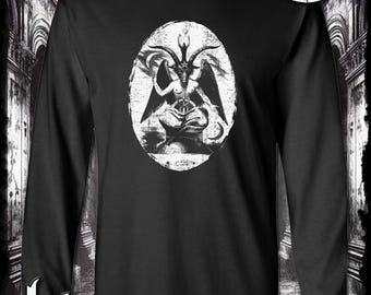 May include: Black long-sleeve t-shirt with a white graphic of a horned figure in a circle. The graphic is a stylized depiction of a demon or devil. The shirt has the text "Kinsman Trading Co. LLC" printed on the bottom.