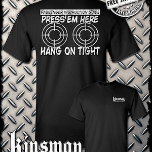 May include: Black t-shirt with white text that reads "Passenger Instruction Guide Press'em Here" with two target symbols and "Hang On Tight". The back of the shirt has a small white logo that reads "Kinsman Trading Co. LLC".