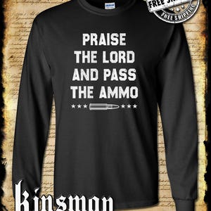 May include: Black long-sleeved shirt with the white text "PRAISE THE LORD AND PASS THE AMMO". A bullet graphic is centered below the text, with stars on either side. The shirt also features the Kinsman trading co. llc logo.