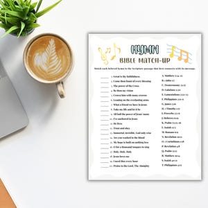 Pu&ograve; includere: Un foglio bianco con il testo "HYMN BIBLE MATCH-UP" e un gioco di abbinamento. Un laptop, una tazza di caff&egrave; con latte art e una piccola pianta verde sono su una superficie bianca.