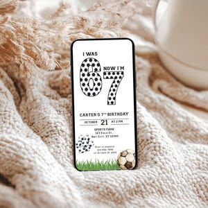 May include: A smartphone displays a soccer-themed birthday invitation. The black and white design features the text "I WAS 6, NOW I'M 7" with soccer ball graphics. The invitation includes event details like date, time, and location.