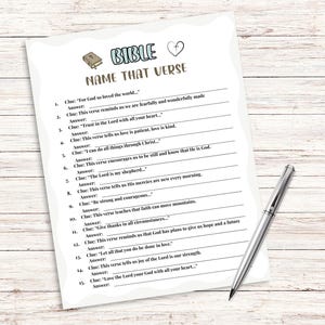 Pu&ograve; includere: Un foglio di carta bianco intitolato "BIBLE NAME THAT VERSE" con una penna su una superficie di legno chiaro. Il foglio presenta indizi di versetti biblici con spazi per le risposte. Un libro e un cuore in alto.