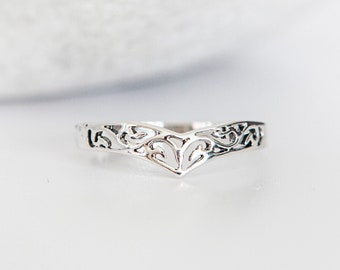 May include: A silver ring with a delicate, intricate design in the shape of a V. The ring is made of a thin band with a cutout pattern that resembles leaves and swirls.
