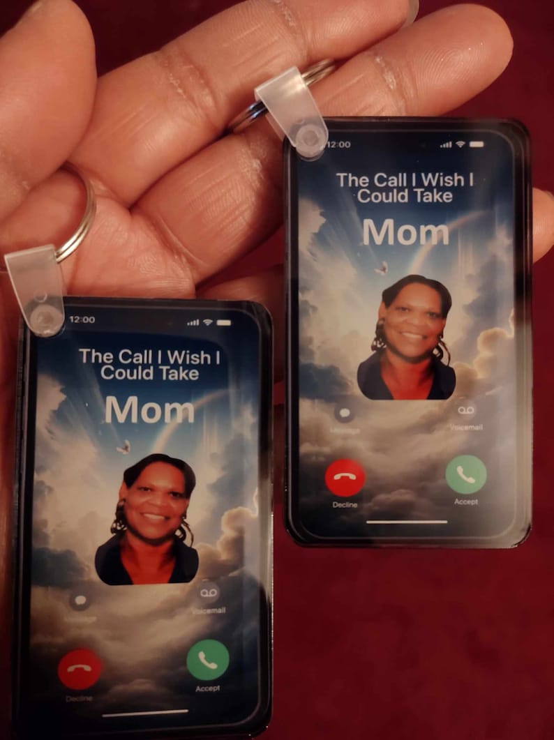 May include: Two keychains shaped like smartphones, each displaying a photo and the text "The Call I Wish I Could Take Mom." The screen shows a sky background and call buttons. The keychains are held by a hand.