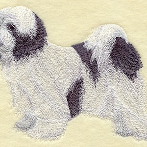 Puede incluir: Un perro tibetano terrier blanco y negro con pelo largo y esponjoso. El perro está acostado con la cabeza girada hacia un lado.