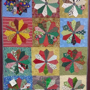 May include: A quilt with a patchwork design featuring 12 colorful pinwheels. Each pinwheel is made of various fabrics in shades of red, green, white, and yellow. The pinwheels are arranged in a grid pattern on a background of blue, brown, and beige fabric.