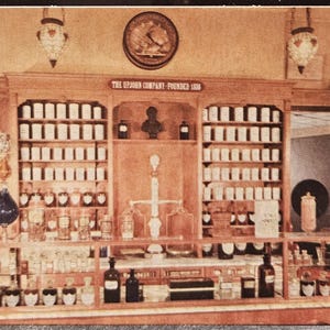 May include: An antique pharmacy interior with wooden shelves filled with white jars and glass bottles. The sign above reads "The Upjohn Company - Founded 1886". Decorative lamps hang from the ceiling, and a scale is visible.