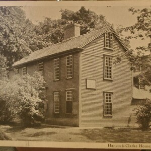 May include: A black and white vintage postcard image of a historic house with a wooden exterior and multiple windows. The house is surrounded by trees and bushes. The text "Hancock-Clarke House, Lexington, Mass." is printed at the bottom of the postcard.