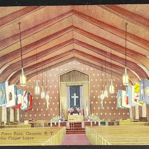 May include: A vintage postcard showing the interior of a chapel at Sampson Air Force Base in Geneva, New York. The chapel has a wooden vaulted ceiling and rows of pews. The altar is decorated with flowers and a cross. Flags representing different branches of the military hang from the ceiling.