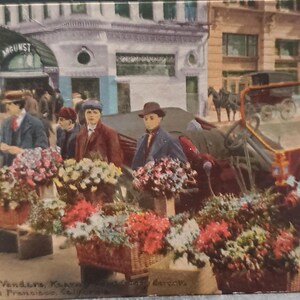 May include: A vintage postcard depicting a street scene in San Francisco, California.  The image shows a group of flower vendors selling bouquets of flowers from baskets on the sidewalk.  A horse-drawn carriage is parked in the background.  The postcard reads "Flower Vendors, Kearny St., San Francisco, Cal."