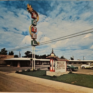 Pode incluir: Postal vintage com um motel e uma placa iluminada alta que diz "MOTEL". A placa tem uma estrela no topo e está situada contra um céu nublado. Uma placa para "Molly Gibson Restaurant & Lounge" também é visível.