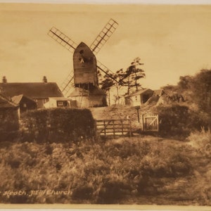 May include: A black and white vintage postcard showing a windmill on a hill with a few houses in the foreground. The text on the postcard reads "Reigate Heath, New Church".