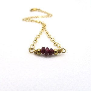 May include: A delicate gold chain bracelet with a small cluster of red gemstone beads.