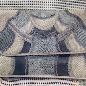 May include: A rectangular clutch with a flap closure, featuring a snakeskin pattern in shades of gray, blue, and beige. The bag has a shoulder strap and a textured appearance, suggesting a vintage or handcrafted design.