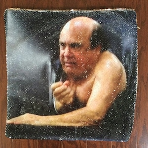 May include: A black and white sequin pillow with a close-up image of a man with a serious expression. The man is shirtless and has a bald head.
