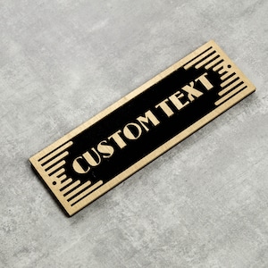 May include: A gold-colored wooden sign with black text that reads "CUSTOM TEXT" in a decorative font. The sign has a geometric pattern around the edges.
