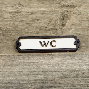 Peut inclure: Une plaque noire et blanche avec les lettres "WC" sur un fond en bois.