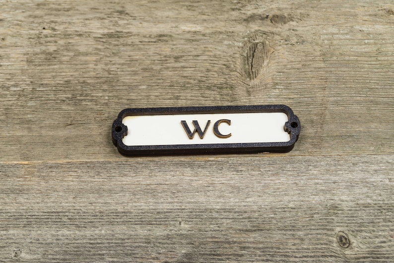 Peut inclure: Une plaque noire et blanche avec les lettres "WC" sur un fond en bois.