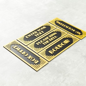 May include: Five black and gold rectangular signs with gold lettering. The signs read "Box Office", "Enter Your Text", "Please Ring The Bell", "Boudoir", and "Will It Go On".