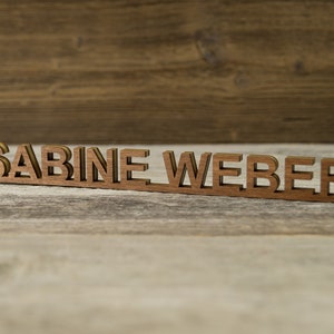 May include: Wooden nameplate with the name "SABINE WEBER" in a brown wood finish.