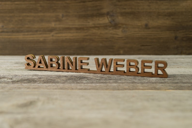 May include: Wooden nameplate with the name "SABINE WEBER" in a brown wood finish.