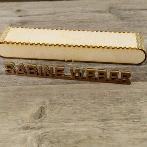 May include: A wooden box with a decorative edge and the name "SABINE WEBER" spelled out in wooden letters.