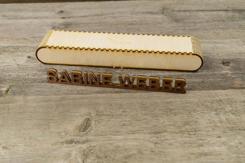 May include: A wooden box with a decorative edge and the name "SABINE WEBER" spelled out in wooden letters.