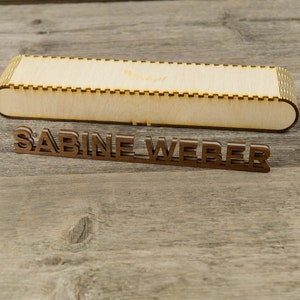 May include: A wooden box with a decorative edge and the name "SABINE WEBER" engraved on the front.